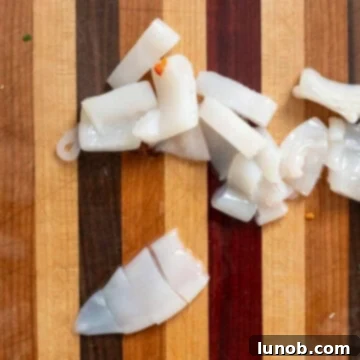 Ebony Ocean Pasta with Seared Calamari 4 Hands slicing cleaned squid tubes into rings on a cutting board.