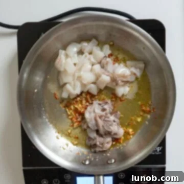 Ebony Ocean Pasta with Seared Calamari 6 Sliced calamari being stirred into a saucepan with garlic, chili, and anchovies.