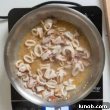 Ebony Ocean Pasta with Seared Calamari 7 White wine being poured over calamari, garlic, chili, and anchovies in a saucepan.