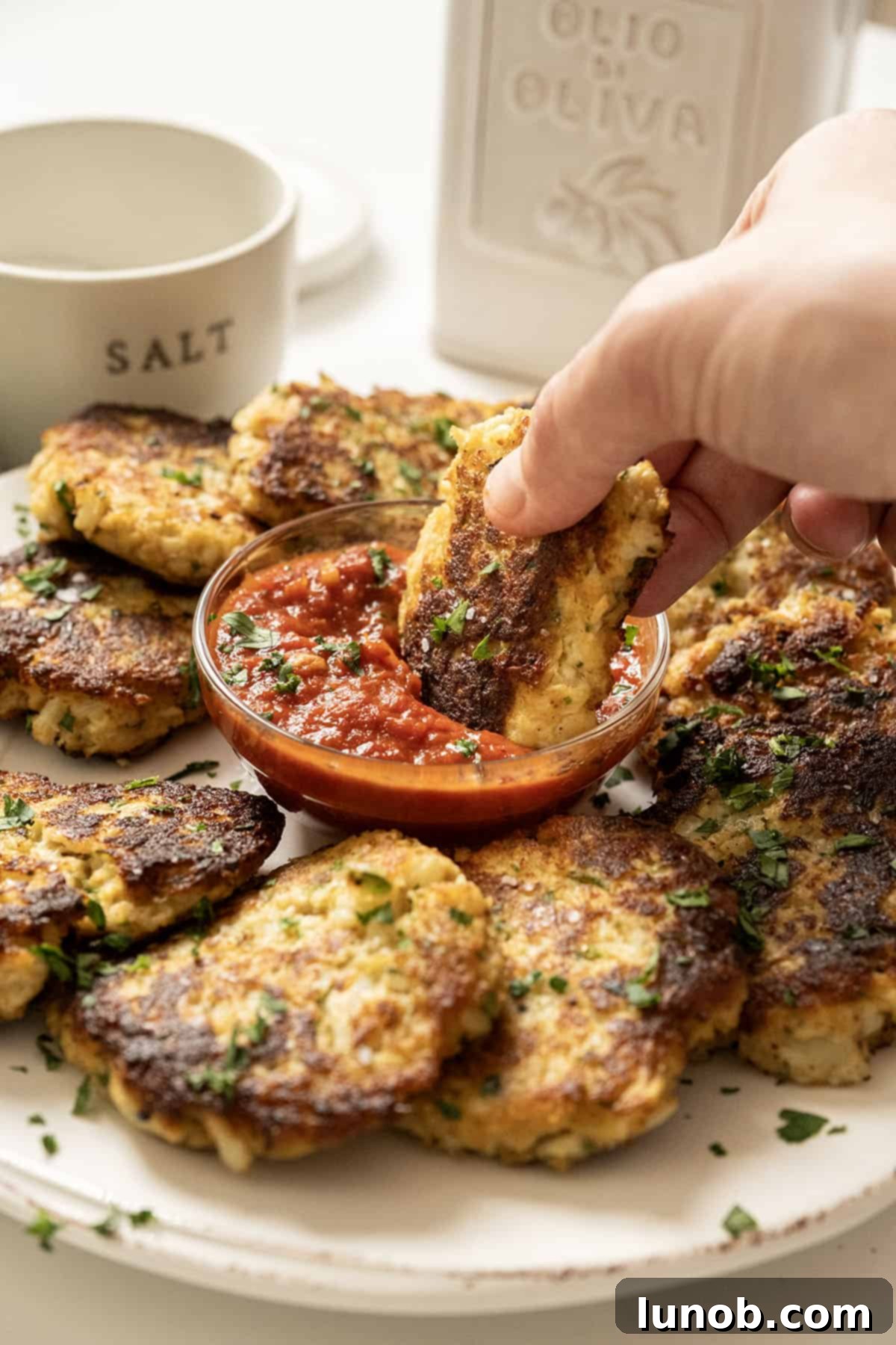 Crispy Cauliflower Fritters 2 Fried cauliflower cakes on a plate with marinara sauce.