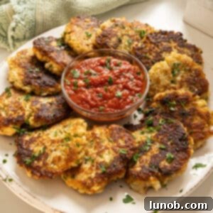Crispy Cauliflower Fritters 12 Fried cauliflower cakes on a plate with marinara sauce.