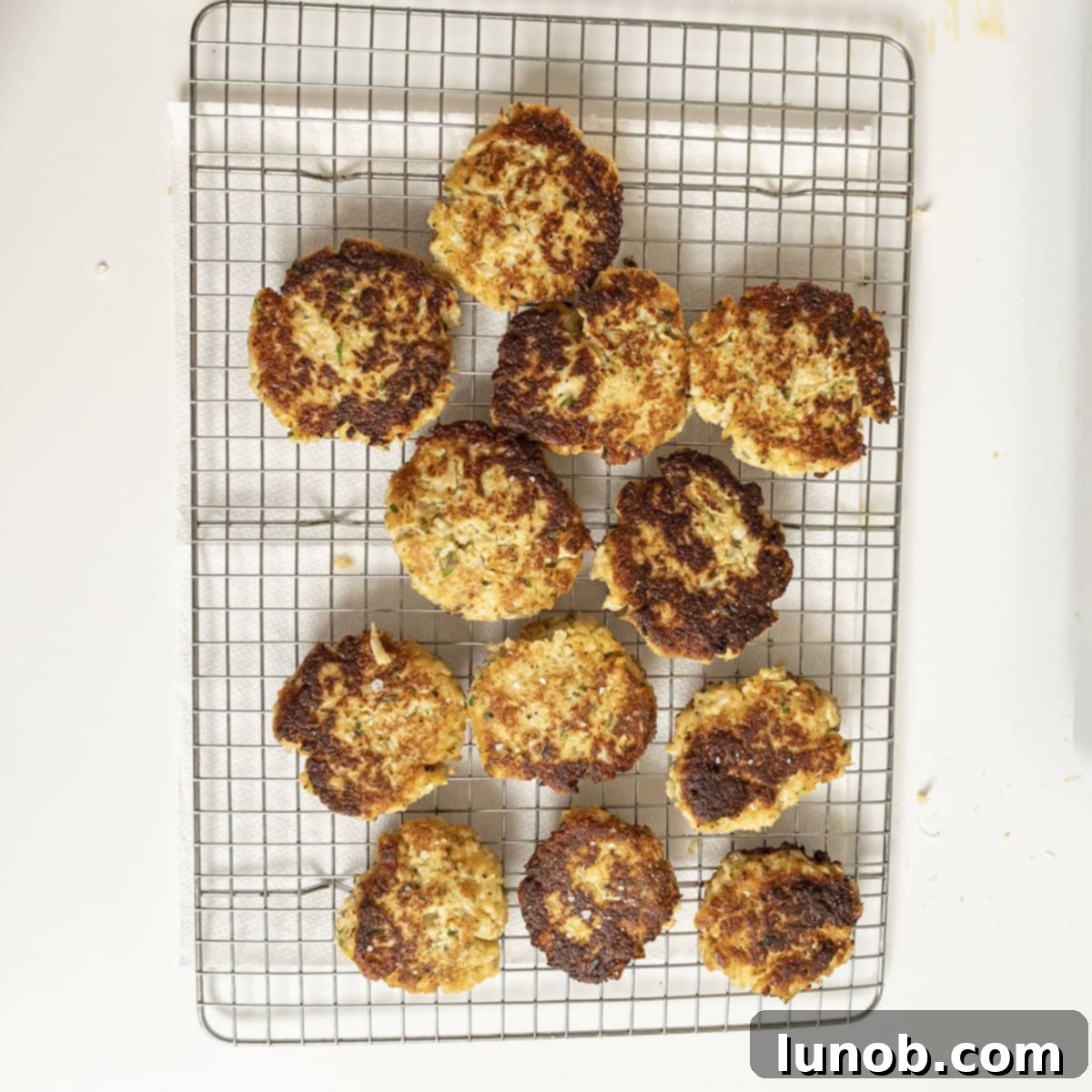 Crispy Cauliflower Fritters 10 Fried cauliflower cakes on a cooling rack, sprinkled with salt.