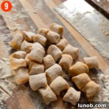 Freshly cut homemade pumpkin gnocchi scattered on a wooden cutting board, lightly dusted with flour.