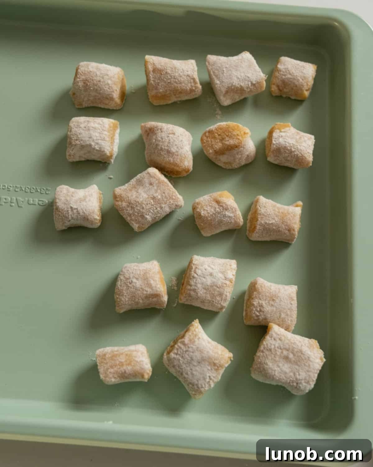 Multiple homemade pumpkin gnocchi pieces spread out in a single layer on a baking tray, ready for freezing.