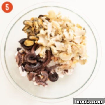Various cooked seafood types are gathered in a large mixing bowl, ready for the next steps of the salad preparation.