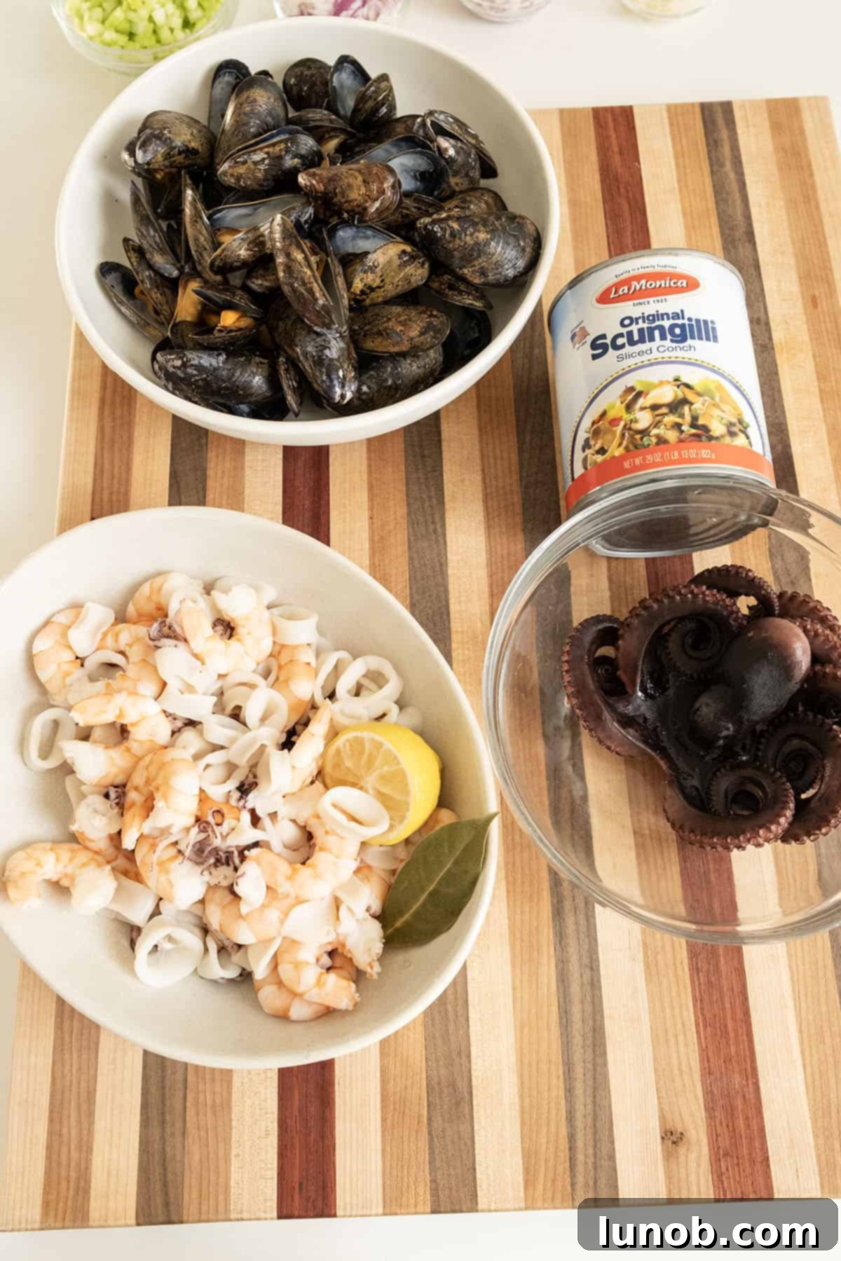 Assorted cooked seafood, including octopus, shrimp, and calamari, laid out on a cutting board, ready to be chopped for the salad.